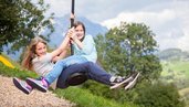 Zwei Maedchen schingen durch den Spielplatz auf dem Schwingeil im Kinderhotel Sailer in Tirol.