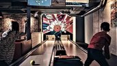 Ein Kind spielt in der Playfactory des Familienhotel Mia Alpina in Tirol Bowling auf einer Bahn mit Monitoren und buntem Licht.