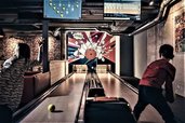 Ein Kind spielt in der Playfactory des Familienhotel Mia Alpina in Tirol Bowling auf einer Bahn mit Monitoren und buntem Licht.