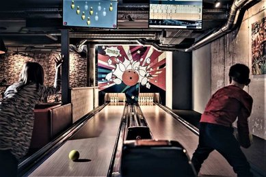 Ein Kind spielt in der Playfactory des Familienhotel Mia Alpina in Tirol Bowling auf einer Bahn mit Monitoren und buntem Licht.