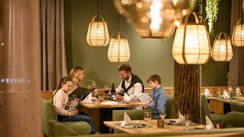 Familie sitzt im Restaurant des Zauchenseehofs an einem gemütlich beleuchteten Tisch, studiert die Speisekarte und genießt die warme, stimmungsvolle Atmosphäre.