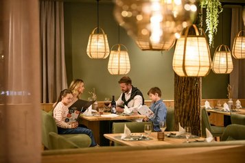 Familie sitzt im Restaurant des Zauchenseehofs an einem gemütlich beleuchteten Tisch, studiert die Speisekarte und genießt die warme, stimmungsvolle Atmosphäre.
