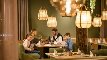 Familie sitzt im Restaurant des Zauchenseehofs an einem gemütlich beleuchteten Tisch, studiert die Speisekarte und genießt die warme, stimmungsvolle Atmosphäre.