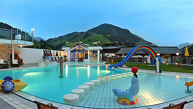 Pool mit Kinderrutsche und anderen Spielmöglichkeiten mit ausblick auf die Berge im Familienhotel Wellness- & Familienhotel Egger in Saalbach Hinterglemm.
