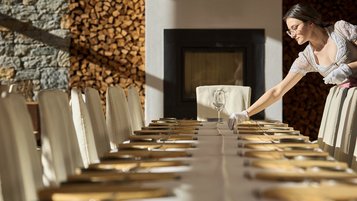 Mitarbeiterin deckt einen festlich vorbereiteten Tisch im Restaurant des Familienhotel Bella Vista Südtirol.