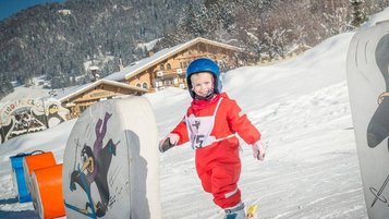 Ein strahlendes Kind in rotem Skianzug macht erste Schwünge in der liebevoll gestalteten Kinderskischule im Landgut Furtherwirt