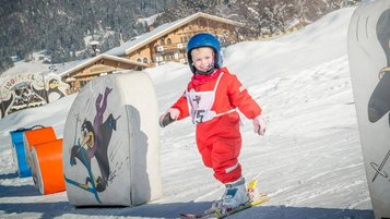 Ein strahlendes Kind in rotem Skianzug macht erste Schwünge in der liebevoll gestalteten Kinderskischule im Landgut Furtherwirt