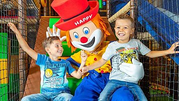 Zwei Kinder haben Spaß in der Softplayanlage mit Maskottchen Happy im Familienhotel Alphotel Tyrol in Südtirol.