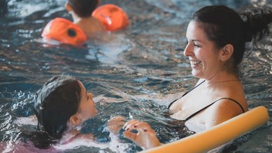 Mutter und Tochter planschen gemeinsam lachend im warmen Innenpool des Familienhotels Amiamo – unbeschwerte Familienzeit im Wasser.