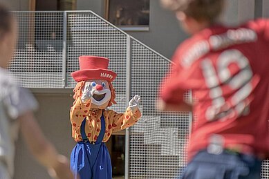 Maskottchen Happy spielt mit den Kindern in der Kinderbetreuung des Familienhotels Gorfion Fußball