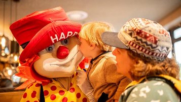 Das Familotel Maskottchen Happy sitzt im Restaurant am Tisch einer Familie im Familienhotel Landhaus zur Ohe im Bayerischen Wald.