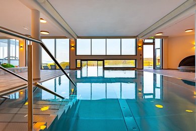 Moderner Indoor-Pool im Familienhotel Petschnighof mit großen Panoramafenstern und Blick in die Natur.