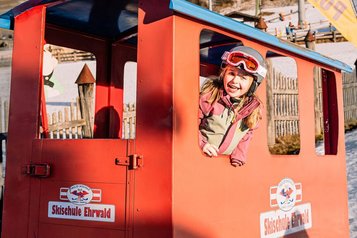 Ein fröhliches Mädchen spielt in einem roten Spielzug der Skischule Ehrwald beim Familienhotel Tirolerhof