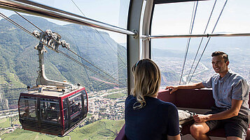 Ein Paar in einer Gondel beobachtet eine andere. Rauf geht es auf einen Berg in Südtirol zum Wandern und Aussicht genießen.