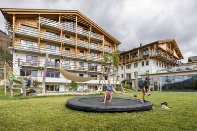 Kinder spielen und toben auf dem Außenspielplatz mit Trampolin vor dem Familienhotel Almfamilyhotel Scherer in Osttirol.