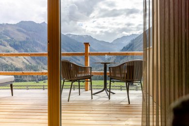 Sonnige Terrasse des Familienhotels Almfamilyhotel Scherer mit Bergblick und gemütlicher Sitzgelegenheit aus Holz und Metall.