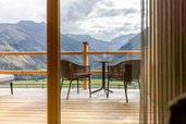 Sonnige Terrasse des Familienhotels Almfamilyhotel Scherer mit Bergblick und gemütlicher Sitzgelegenheit aus Holz und Metall.