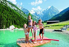 Kinder stehen im Badesee auf einem Floß im Familienhotel Bella Vista in Südtirol.