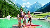Kinder stehen im Badesee auf einem Floß im Familienhotel Bella Vista in Südtirol.