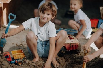 Kinder spielen im Sandbereich des Familienhotels Oberkarteis im Salzburger Land mit Schaufel und Spielzeug.
