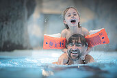 Vater planscht mit seiner Tochter auf den Schultern im Indoor-Pool des Familienhotels Alpenhof Dolomit Family