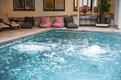 Sprudelndes Wasser im Indoor-Pool des Familienhotels Bruckwirt mit gemütlichen Sitzsäcken und Relaxliegen am Beckenrand.