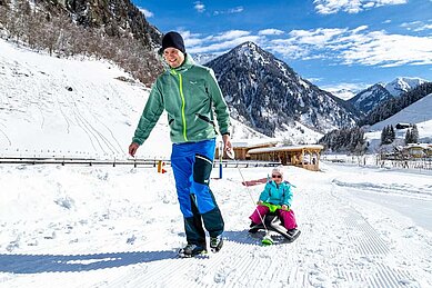 Vater zieht seine Tochter auf dem Schlitten durch die verschneite Landschaft rund um das Familienhotel Oberkarteis