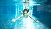 Mädchen taucht mit ausgestreckten Armen durch einen klaren Swimmingpool.