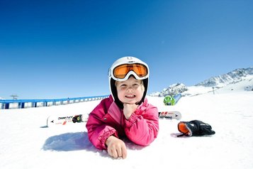 Kleinkind sitzt auf einer Schaukel auf dem Outdoor-Spielplatz des Familienhotels Alpenhotel Kindl in Tirol.