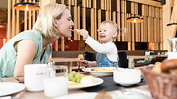 Mutter und Kind essen gemeinsam im Familienhotel. Kind füttert Mutter mit einem Stück Käse. 