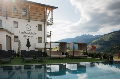 Der Außenpool des Familienhotels Scherer mit gemütlichen Liegen und Panoramablick auf die Berge.