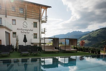 Der Außenpool des Familienhotels Scherer mit gemütlichen Liegen und Panoramablick auf die Berge.