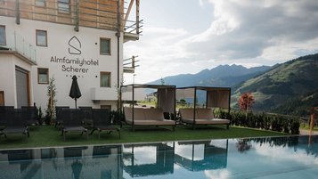 Der Außenpool des Familienhotels Scherer mit gemütlichen Liegen und Panoramablick auf die Berge.