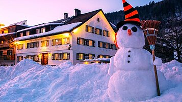 Winteraufnahme des Familienhotels Sonne Bezau mit einem selbstgebautem Schneemann.