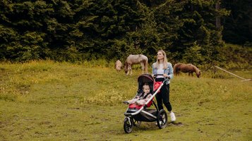 Mutter wandert mit ihrem Kind im Kinderwagen über ein Feld im Salzburger Land.