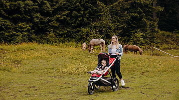 Mutter wandert mit ihrem Kind im Kinderwagen über ein Feld im Salzburger Land.