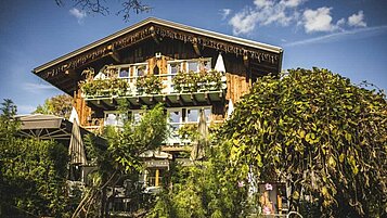 Traditionelles alpines Holzhaus mit reich bepflanztem Balkon, umgeben von üppigem Grün und Steinmauern, strahlt ländlichen Charme aus und lädt zum Verweilen in idyllischer Umgebung ein.