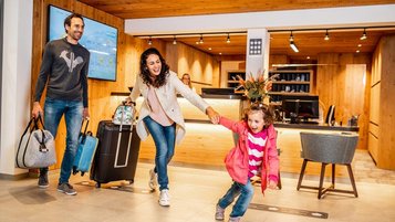 Kleines Kind steht mit Gepäck an der Rezeption im Familienhotel Das Bayrischzell in Oberbayern.