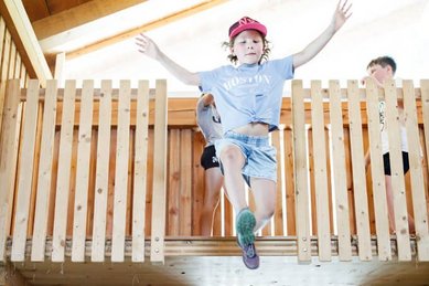 Kind springt von einer Holzplattform in eine Heuscheune im Familienhotel Huber in Südtirol