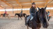 Mädchen sitzt auf einem Pferd und reitet in der Reithalle des Familienhotels Landhaus zur Ohe.