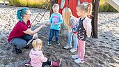 Kinderbetreuerin spiel mit Kindern im Sandkasten auf dem Outdoorspielplatz des Familienhotels Seeklause an der Ostsee.