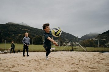 Kinder spielen Beachvolleyball beim Hotel Sonngastein im Salzburger Land auf einem Sandplatz vor Bergkulisse.