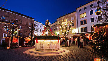Salzburger Land Ausflugstipps im Winter: Gemeinsam über den Halleiner Adventsmarkt schlendern. Der Brunnen in der Mitte des Platzes ist weihnachtlich geschmückt, drumherum stehen verschiedene Buden.. 