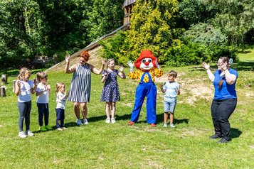 Kinderbetreuer vom Familys Club Harz spielen draußen auf der Wiese mit Maskottchen Happy und den Kindern. 