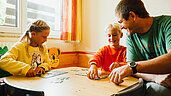 Kinder spielen im Spielzimmer mit einem Betreuer Puzzle im Familienhotel Kinderhotel Sailer in Pitztal.