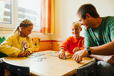 Kinder spielen im Spielzimmer mit einem Betreuer Puzzle im Familienhotel Kinderhotel Sailer in Pitztal.