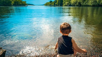 Kleinkind sitzt am Seeufer und planscht mit den Händen im Wasser.