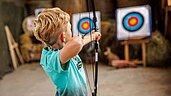 Junge zielt mit Pfeil und Bogen auf eine Zielscheibe.
