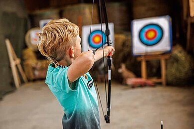 Junge zielt mit Pfeil und Bogen auf eine Zielscheibe.