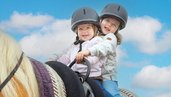 Zwei Kinder sitzen auf einem Pferd und lächeln in die Kamera im Familienhotel Familien Resort Petschnighof in Kärnten.